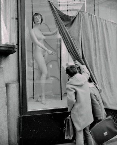 18 Mar 1956, Rome, Italy --- Two curious Rome school children pull back the curtain to get a glimpse of a forbidden sight. The surprised young lady seems to be pointing the way out for these indiscreet youngsters, peering into a shop window while it was being redecorated. After all, even a department store mannequin has a right to some privacy!